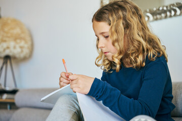 Young girl drawing on notepad while sitting on sofa at home