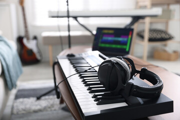 MIDI keyboard, laptop and headphones on wooden table in home studio, selective focus