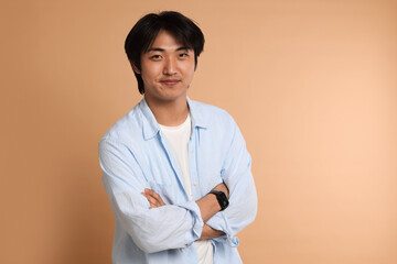 Portrait of handsome Asian man with crossed arms on beige background