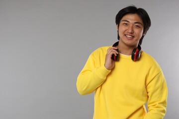 Smiling Asian man with headphones on grey background. Space for text