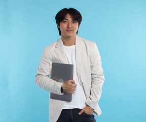 Handsome Asian businessman in suit with laptop on light blue background