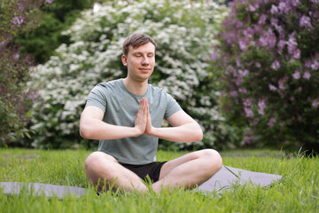 Young man practicing yoga on mat in park