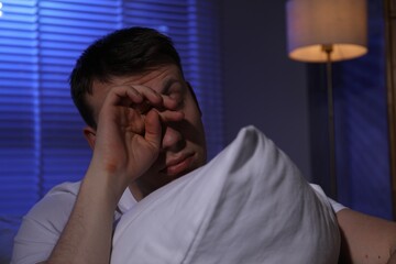 Frustrated man with pillow suffering from insomnia indoors