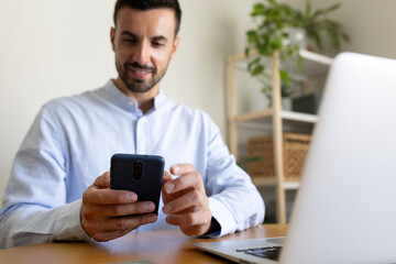 Man using smart phone, sending text message while working at home office. Selective focus.