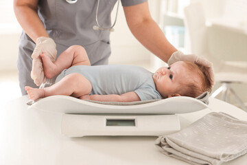 Pediatrician weighting baby with scales at white table in clinic, closeup