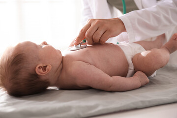 Pediatrician examining baby with stethoscope at table in clinic, closeup