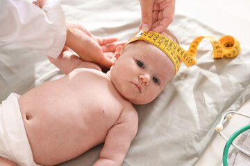 Pediatrician measuring baby's head with tape at table in clinic, closeup