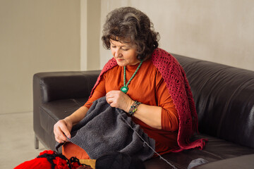Elderly woman enjoys knitting with wool on a cozy sofa in a modern living space