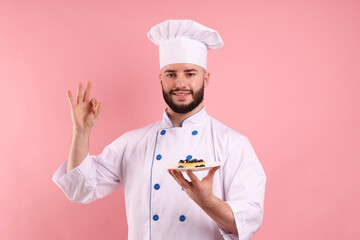 Happy confectioner in uniform holding tart with blueberries and showing ok gesture on pink...