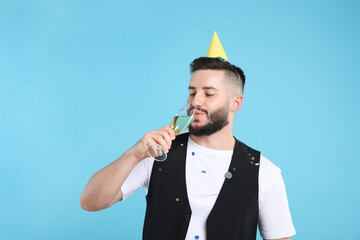 Happy Birthday. Handsome man with party hat and glass of champagne on light blue background