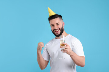 Happy Birthday. Handsome man with party hat and glass of champagne on light blue background, space...