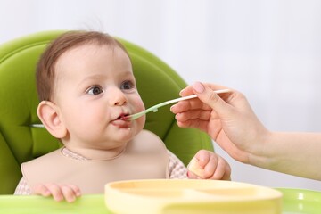 Mother feeding her baby on chair at home, closeup