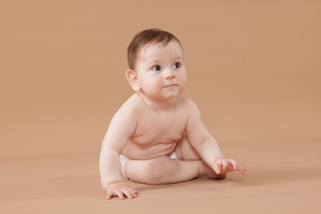 Cute little baby in diaper sitting on beige background