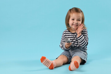 Cute little girl with microphone on light blue background, space for text