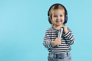 Cute little girl with headphones and microphone on light blue background, space for text