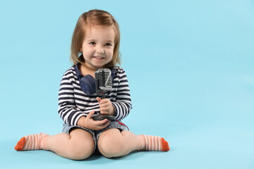 Cute little girl with headphones and microphone on light blue background, space for text