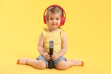 Cute little girl with headphones and microphone on yellow background
