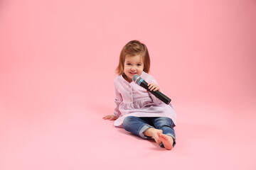 Cute little girl with microphone on pink background