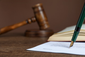 Signing notary document with fountain pen at wooden table against brown background, closeup