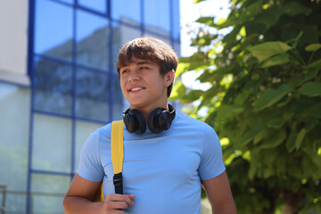 Smiling teenage boy with headphones on city street, low angle view