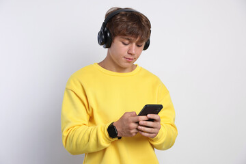 Cute teenage boy in headphones with smartphone on light grey background