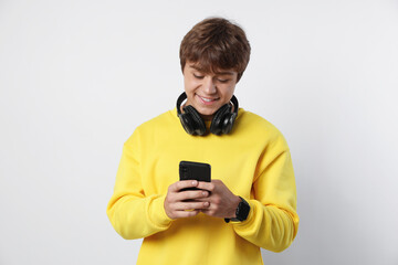 Smiling teenage boy with headphones and smartphone on light grey background
