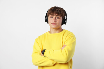 Portrait of cute teenage boy in headphones with crossed arms on light grey background