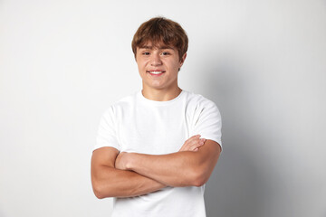Portrait of smiling teenage boy with crossed arms on light grey background