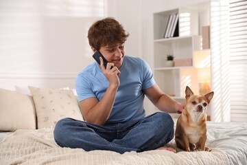 Smiling teenage boy talking by smartphone and dog on bed at home
