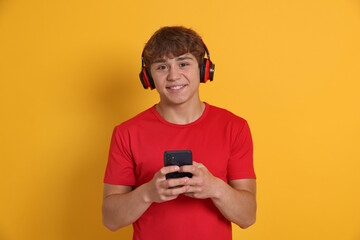 Smiling teenage boy in headphones with smartphone on yellow background