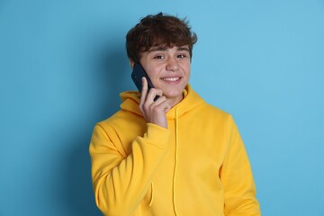 Portrait of smiling teenage boy talking by smartphone on light blue background