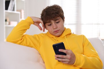 Teenage boy using smartphone on sofa at home