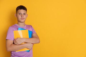 Teenage boy with notebooks on orange background, space for text
