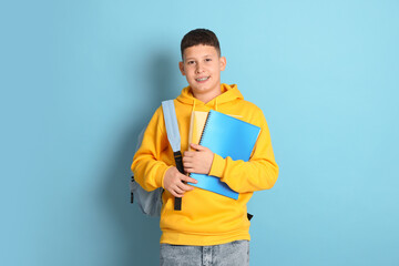 Teenage boy with backpack and notebooks on light blue background