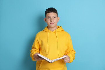 Teenage boy reading book on light blue background
