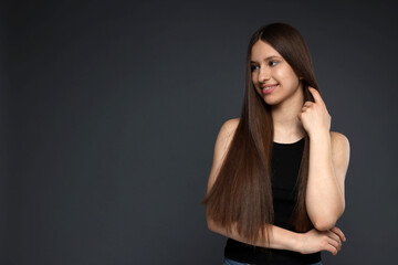 Smiling teenage girl with healthy long hair on dark grey background. Space for text