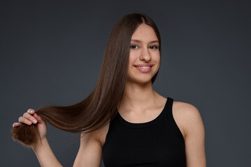 Portrait of smiling teenage girl with healthy long hair on dark grey background