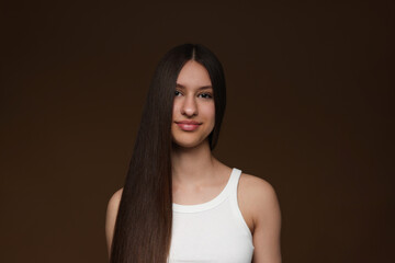 Portrait of beautiful teenage girl with healthy long hair on brown background