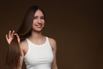 Portrait of smiling teenage girl with healthy long hair on brown background. Space for text
