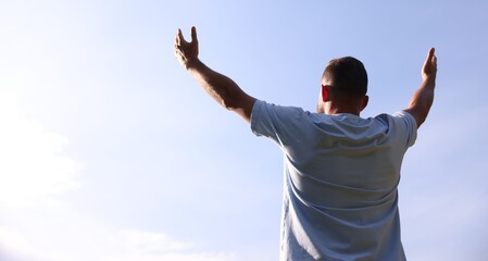 Feeling freedom. Man enjoying time outdoors against blue sky, back view. Space for text