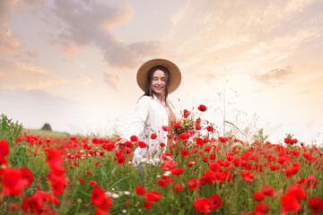 Smiling woman in hat picking wildflowers in meadow