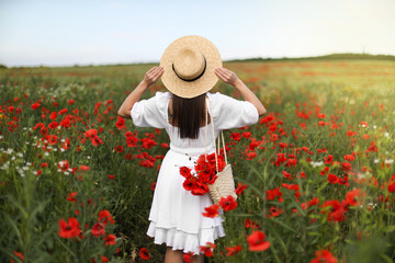 Woman in hat with bag of poppy flowers in wildflower meadow, back view