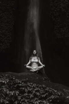 Young woman meditating in front of majestic waterfall in lush jungle