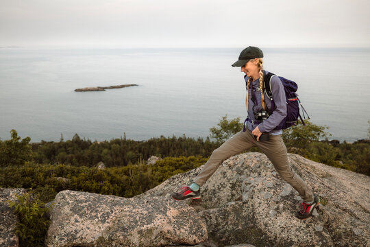Woman hops from rock to rock while hiking in Acadia National Park