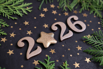 Gold numbers 2026 with star instead of the number 0 are located on black background with small gold stars and green fir branches. and Ideal for holiday greetings, New Year's holidays or winter design
