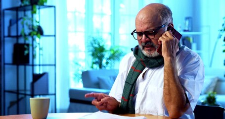 Indian senior man discussing tax report on phone with CA at home at table, happy elderly person smiling while consulting chartered accountant about financial documents during income tax filing season