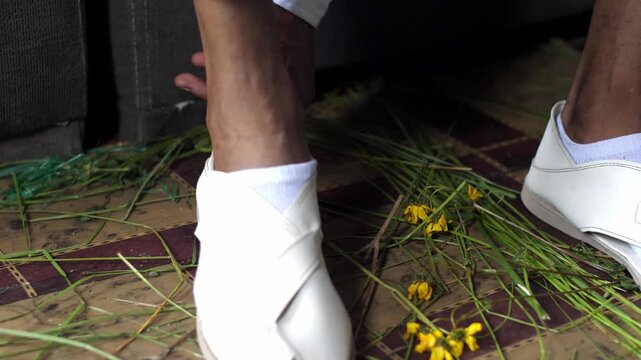 Close-up of man putting on white ceremonial sandals over grass mat in Kara Kotobe