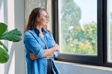 Middle aged calm beautiful woman looking out window