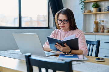 Middle-aged serious woman working at computer laptop in home office