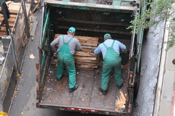 Two workers load lumber into a city garbage truck